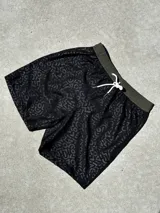 Short de baño negro con estampado de letras y figuras geométricas en gris oscuro. Cintura elástica con cordón ajustable blanco y ribete verde oliva.