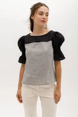 Blusa de rayas horizontales grises y blancas, con mangas abullonadas cortas negras y escote redondo.