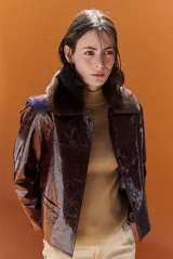 Chaqueta de efecto cuero brillante con acabado charol, cuello con solapas de piel sintética, cierre frontal con botones y bolsillos laterales.
