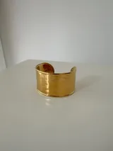 Brazalete rígido tipo cuff de diseño ancho, con acabado metálico dorado y textura ligeramente irregular.