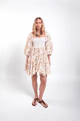 Vestido corto de encaje color beige, con cuerpo fruncido elastizado, escote recto y mangas abullonadas. La falda con volados resalta la textura del encaje.