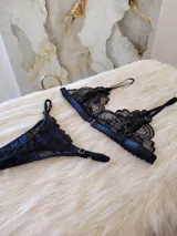 Conjunto de lencería compuesto por un bralette de encaje con breteles regulables y una tanga regulable con corte cola less. Ambas piezas presentan un diseño de encaje floral negro.