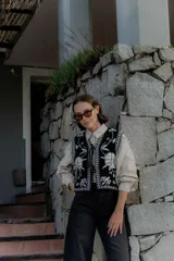 Chaleco tejido de punto con diseño floral en contraste, cierre frontal con lazos y terminaciones con guardas geométricas.