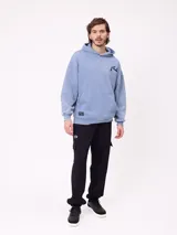 Canguro con capucha de calce holgado, color azul con efecto lavado. Presenta bolsillo frontal tipo canguro, logo de la marca estampado en el pecho y etiqueta pequeña en el ruedo.