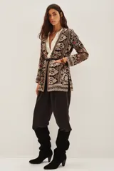 Saco sastrero con escote en V y mangas largas, confeccionado en gabardina liviana negra con bordados florales y patrones geométricos en tonos beige, dorado y toques de color (fucsia, verde, violeta). Presenta botones ocultos, bolsillos ojal, hombreras y un cinturón fino de cuero negro.