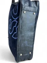 Bolso de mano tipo maletín, confeccionado en cuero natural y gamuza negra con bordado decorativo en tono azul. Cuenta con doble asa superior, cierre principal con doble cursor y base con topes metálicos.