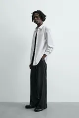 Camisa blanca de corte slim fit, confeccionada en tejido de algodón. Presenta cuello italiano, manga larga con puño abotonado y cierre frontal de botonadura.