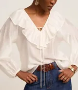 Blusa color blanco confeccionada en voile, de mangas largas con elástico en los puños, cuello en V con volado y lazo con adornos metalizados.