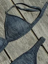 Bikini de dos piezas color marrón, con corpiño triangular fijo con corte bajo el busto, breteles regulables con hebilla y almohadillas desmontables. La bombacha es vedetina con frunce elástico en los costados.