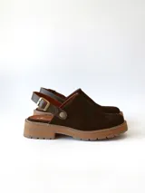 Zueco de cuero gamuzado color chocolate, con diseño de punta cerrada y tira ajustable con hebilla metálica en el talón. Presenta una suela de plataforma dentada en tono marrón claro.