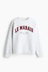 Buzo gris melange con cuello redondo, hombros caídos y puños y bajo acanalados. Estampado frontal en color bordó con el texto "LE MARAIS" y "Ville de Paris 1995".