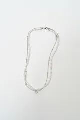 Collar doble de cadena fina plateada y perlas blancas, con un dije central de cristal brillante.
