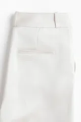 Pantalón sastrero de tiro alto y pierna recta, color blanco, con raya marcada al frente y en la espalda, bolsillos laterales al bies y bolsillos traseros decorativos.