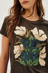 Remera de algodón color marrón oscuro con cuello redondo y manga corta. Estampado frontal con flores blancas y detalles en lentejuelas doradas, hojas verdes y texto en azul oscuro que dice "TRÈS CHIC".