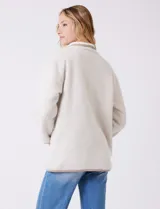 Cardigan beige con diseño de espiga, forrado en corderito sintético blanco. Presenta vivos en contraste color tostado en los bordes, cuello solapa y bolsillos tipo parche con solapa. Cierre frontal con botones carey.