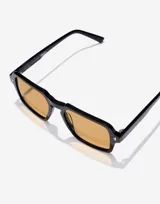 Lentes de sol Hawkers modelo Lash Eco en colaboración con Smiley. Presentan un marco cuadrado de color negro con acabado brillante y cristales en tono ámbar. Incluyen detalles metálicos en las esquinas y el logo de Smiley grabado en las patillas.