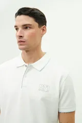 Polo de manga corta con textura, corte regular y cierre frontal con botones. Presenta un logo estampado en el pecho y detalles en color celeste en el cuello y los puños.