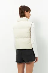 Chaleco puffer color beige, sin mangas, con cuello alto y cierre frontal con cremallera.