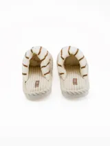 Pantuflas abiertas de estilo mule, con capellada de peluche color crema con rayas negras horizontales y plantilla de pana acanalada en tono beige.