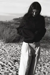 Pantalón negro de tiro alto con pliegues marcados en el delantero y corte ancho en las piernas. Presenta cierre frontal con botón y cremallera, y bolsillos laterales.