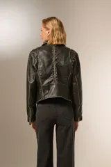 Chaqueta corta de cuero sintético negro con cuello solapa, cierre frontal asimétrico, bolsillos con cierre y tachas plateadas en cuello y hombros.