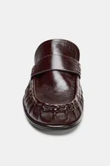 Mocasín tipo mule destalonado en piel color marrón oscuro, con detalle fruncido en la puntera redonda y antifaz en el empeine.