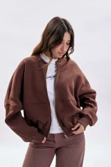 Campera oversize color marrón con cierre frontal, mangas amplias y diseño con cortes horizontales. Presenta puños y ruedo acanalados.