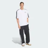 Remera oversized Adidas Adicolor de color blanco, de corte holgado, con cuello redondo, mangas cortas con las icónicas tres tiras negras y el logo Trefoil bordado en el pecho.