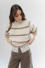 Buzo de tejido de punto grueso con diseño a rayas horizontales en color crudo y marrón. Presenta cuello redondo, mangas largas y un corte holgado.
