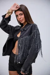 Campera de jean color negro con efecto lavado, de corte oversize, con flecos brillantes integrados en el diseño frontal y en las mangas.