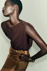 Body de manga larga color marrón oscuro, con escote asimétrico drapeado y detalle de broche metálico en el hombro derecho.