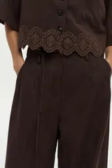 Pantalón de lino marrón de corte ancho y relajado, con pinzas frontales, bolsillos y lazo ajustable en la cintura.