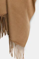 Capa abierta confeccionada en hilatura con lana, de diseño asimétrico con aplicación de flecos en el bajo.