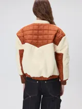 Campera crop de estilo boxy, confeccionada en corderito color crema con paneles acolchados en color terracota en el frente y las mangas. Presenta cuello alto, cierre frontal metálico, puños y ruedo elastizados, y logo de la marca bordado en el pecho.