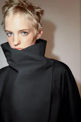 Cazadora corta de color negro con cuello subido cruzado, manga larga con puños anchos ajustados con trabilla y botón, y cierre frontal cruzado con botones ocultos.