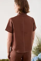 Blusa de lino verde de manga corta y corte recto, con cuello alto con volado y cierre frontal cruzado con botoncitos dorados.