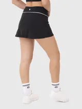 Conjunto deportivo compuesto por un top corto con cuello polo y una pollera short (skort) con detalle de línea blanca en la cintura. Ambas piezas son de color negro y diseño minimalista.