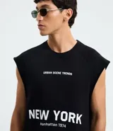 Musculosa masculina de corte boxy fit, confeccionada en algodón. Presenta cuello redondo, hombros ligeramente ampliados y acabado deshilachado en el ruedo. Cuenta con estampa frontal con la frase 'Urban Scene Trends' y el texto 'New York Manhattan 1974' en el centro.