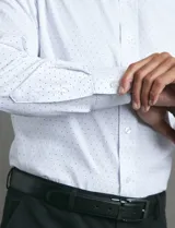 Camisa de vestir de manga larga con cuello rígido y cierre frontal de botones. Presenta un estampado de pequeños puntos azules sobre fondo blanco.