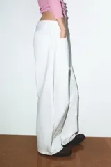 Jeans blancos de tiro medio con cinco bolsillos, detalle de costuras torcidas y cierre frontal con cremallera y botón metálico.