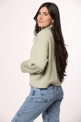 Buzo tejido de punto en color blanco crema, con cuello redondo alto y mangas largas con puños acanalados.