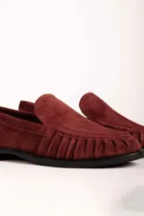 Mocasín de gamuza color bordó con detalle de frunces en la puntera y suela plana de goma negra.