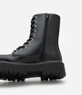 Bota tipo coturno de caña media, confeccionada en poliuretano color negro, con cierre frontal de cordones, cremallera lateral y suela track robusta.