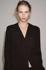 Camisa de lino color negro, de manga larga, con cuello solapa y cierre frontal con botones. Presenta un bolsillo de parche en el delantero.