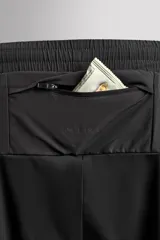 Pantalón negro de entrenamiento slim fit confeccionado en tejido técnico ligero y elástico con estructura. Cuenta con cintura elástica ajustable con cordón, bolsillos frontales y trasero con cierre de cremallera, y bajo ajustable con cremallera en laterales.