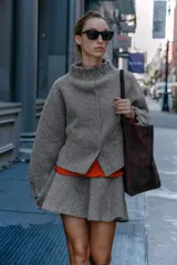Chaqueta estilo bomber de punto color gris, con cuello subido, manga larga y acabados elásticos con frunces en puños y cuello. Cierre frontal con botones a presión ocultos.