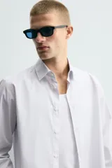 Camisa de corte regular fit confeccionada en tejido de algodón con diseño de rayas verticales finas. Presenta cuello italiano, manga larga con puños abotonados y cierre frontal mediante botonadura.