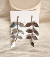 Par de aros colgantes plateados con forma de rama con hojas. Cierre de gancho.
