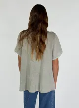 Camisa negra de manga corta con cuello redondo y detalle de volados frontales. Presenta cierre central con botones de madera y terminaciones con puntilla en el escote.
