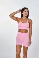 Conjunto deportivo de dos piezas color rosa, compuesto por un top de tirantes finos con logo estampado en el frente y un short de tiro alto con diseño sin costuras.